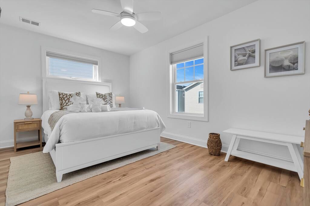 A bedroom with a bed, bedside tables, a ceiling fan, and two windows.