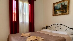 Una cama bien tendida con una colcha marrón, dos toallas y un cuadro de un paisaje forestal en la pared.