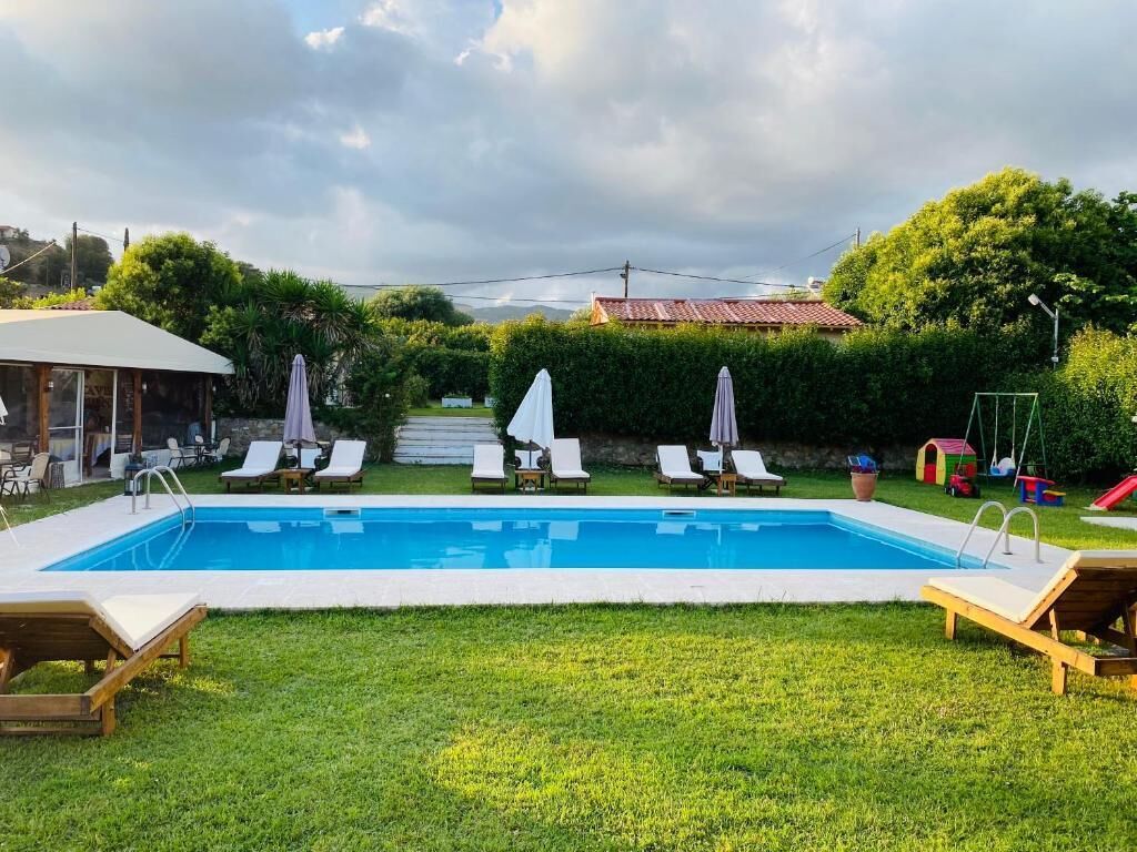 Piscina con sillones de descanso y sombrillas, rodeada de un césped cuidado y una casa al fondo.