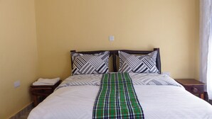 Un lit recouvert d’une couvre-lit blanche à motifs, deux oreillers à dessins géométriques noirs et blancs, et un chemin de lit à carreaux verts.