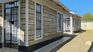 Un bâtiment au design simple et fonctionnel, doté de grandes fenêtres avec des barreaux métalliques, d’une façade en béton et d’un chemin de gravier menant à l’entrée.