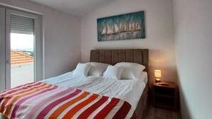 A bedroom with a bed, a painting of sailboats, a window, and a nightstand with a lamp. - Beachfront Apartment With Balcony and Sea View (Vrsi)