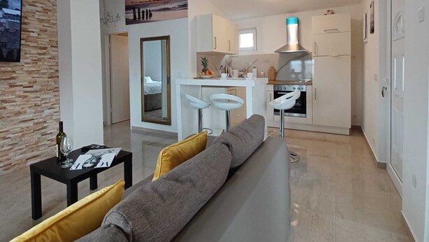 A modern living room with a sofa and a small table, a kitchen with white cabinets and a stove, and a hallway with a mirror and a painting. - Beachfront Apartment With Balcony and Sea View (Vrsi)