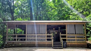 A wooden cabin with a porch, a staircase, and a gravel ground.