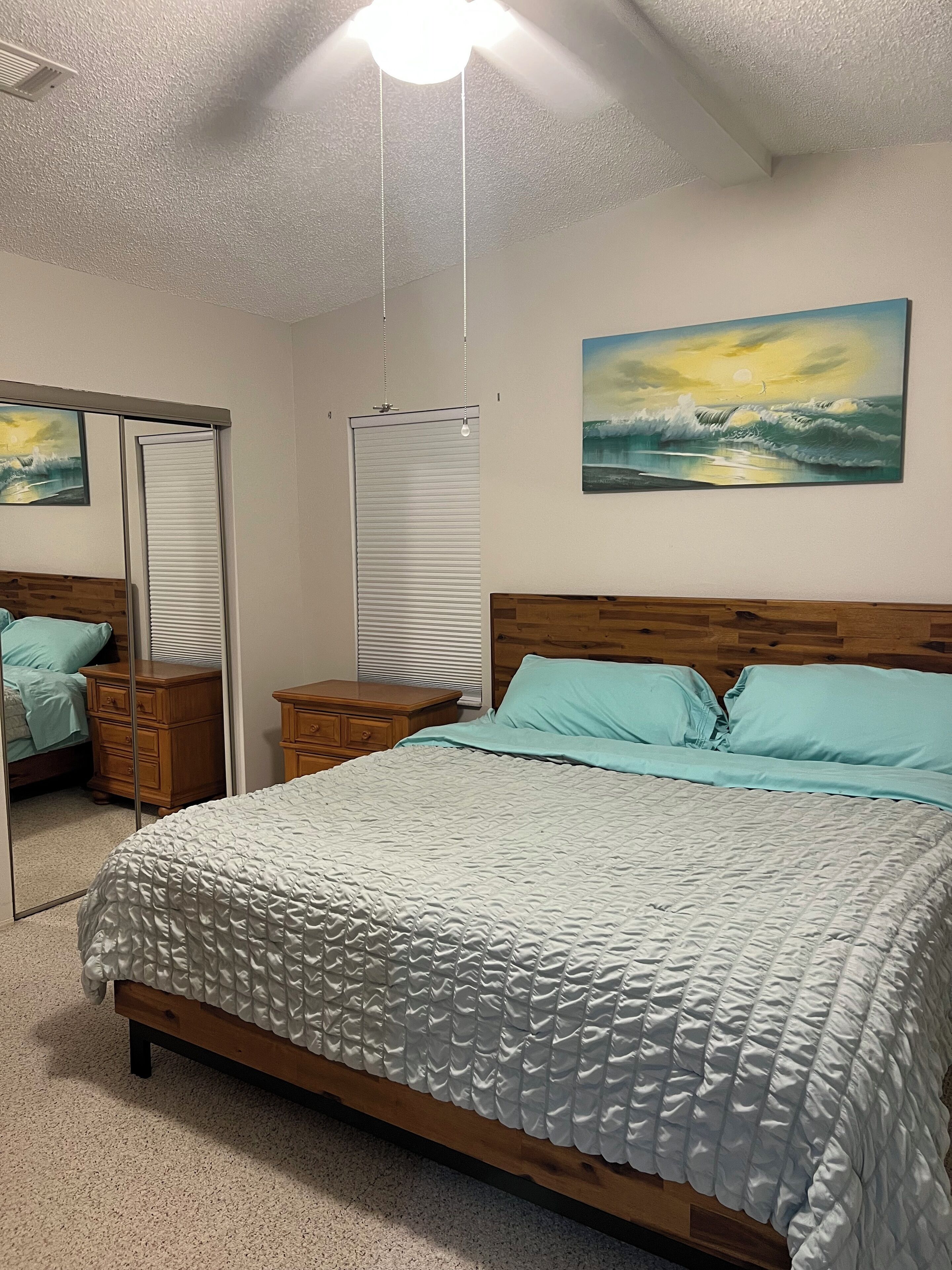 A bedroom with a bed, a nightstand, a dresser, a mirror, and a painting on the wall.