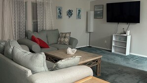 Olohuoneessa on harmaa sohva, puinen sohvapöytä ja seinälle asennettu televisio.