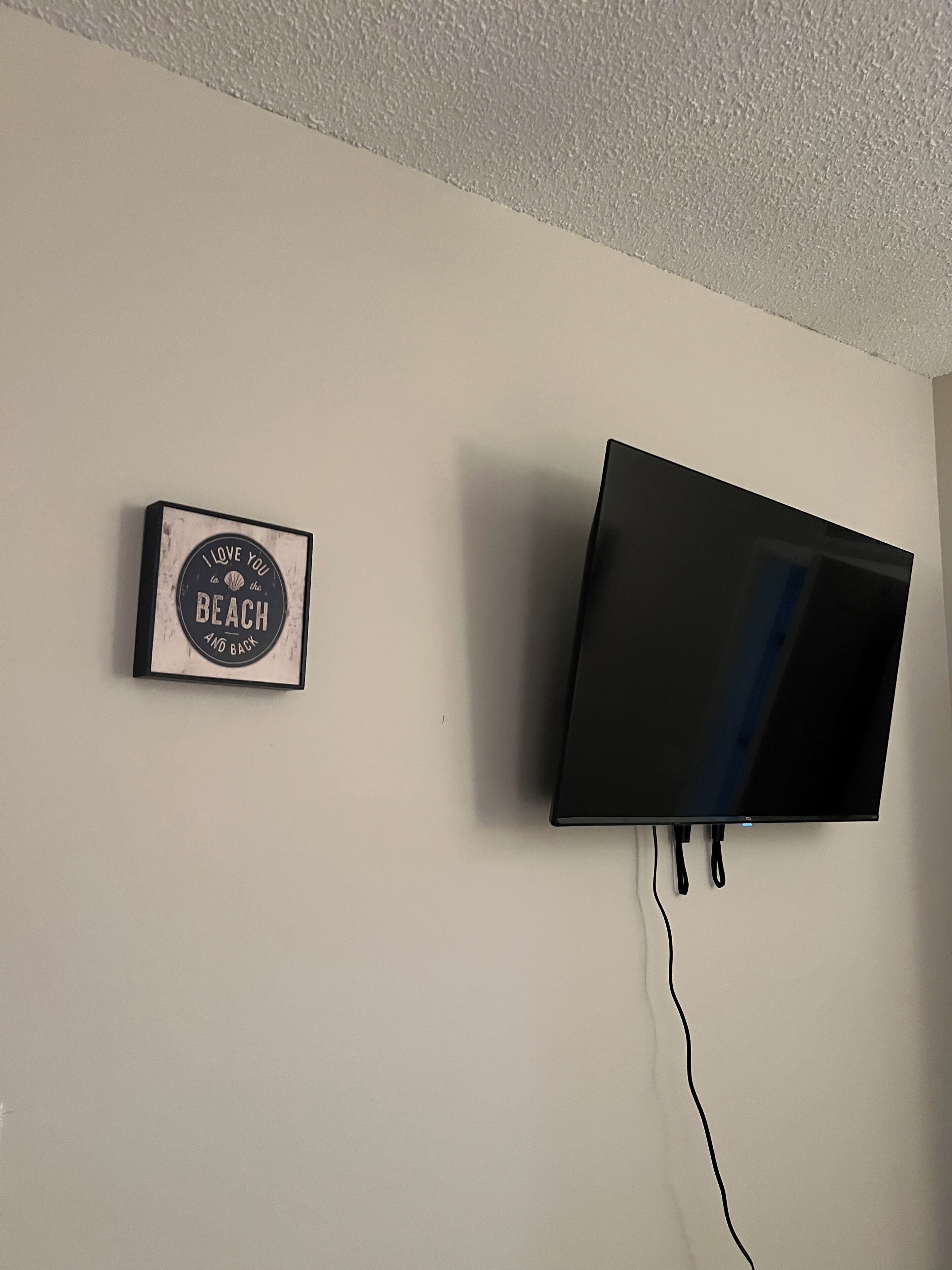 Un téléviseur à écran plat fixé à un mur sobre, avec un seul câble d’alimentation.