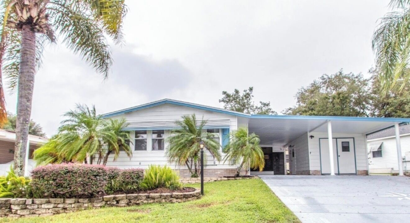 A single-story building with a covered porch, palm trees, and a well-maintained lawn.