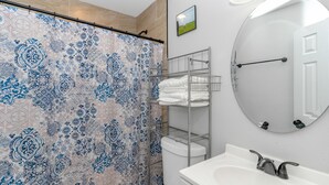 Une salle de bain avec un rideau de douche à motifs, des toilettes, un lavabo avec un miroir et un porte-serviettes.