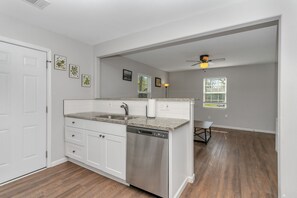 Una cocina con armarios blancos, lavavajillas, encimeras de granito, un fregadero y un ventilador de techo.