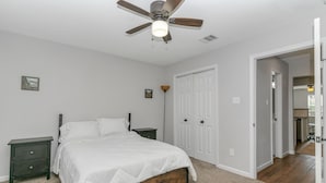 Une chambre à coucher comprenant un lit, une table de chevet, un ventilateur de plafond et une porte donnant sur une autre pièce.