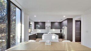 Una cocina moderna con armarios oscuros, una isla central y un comedor con mesa de madera y sillas blancas.