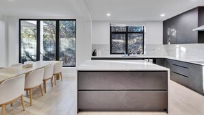 Una cocina moderna con una isla grande, armarios oscuros y amplias ventanas con vistas a árboles.