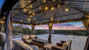 Un área de estar al aire libre cubierta, con mobiliario de mimbre e iluminación con guirnaldas.