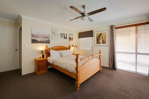 Ein Schlafzimmer mit einem hölzernen Bett, Deckenventilator, Nachttisch und einem Fenster mit Jalousien.