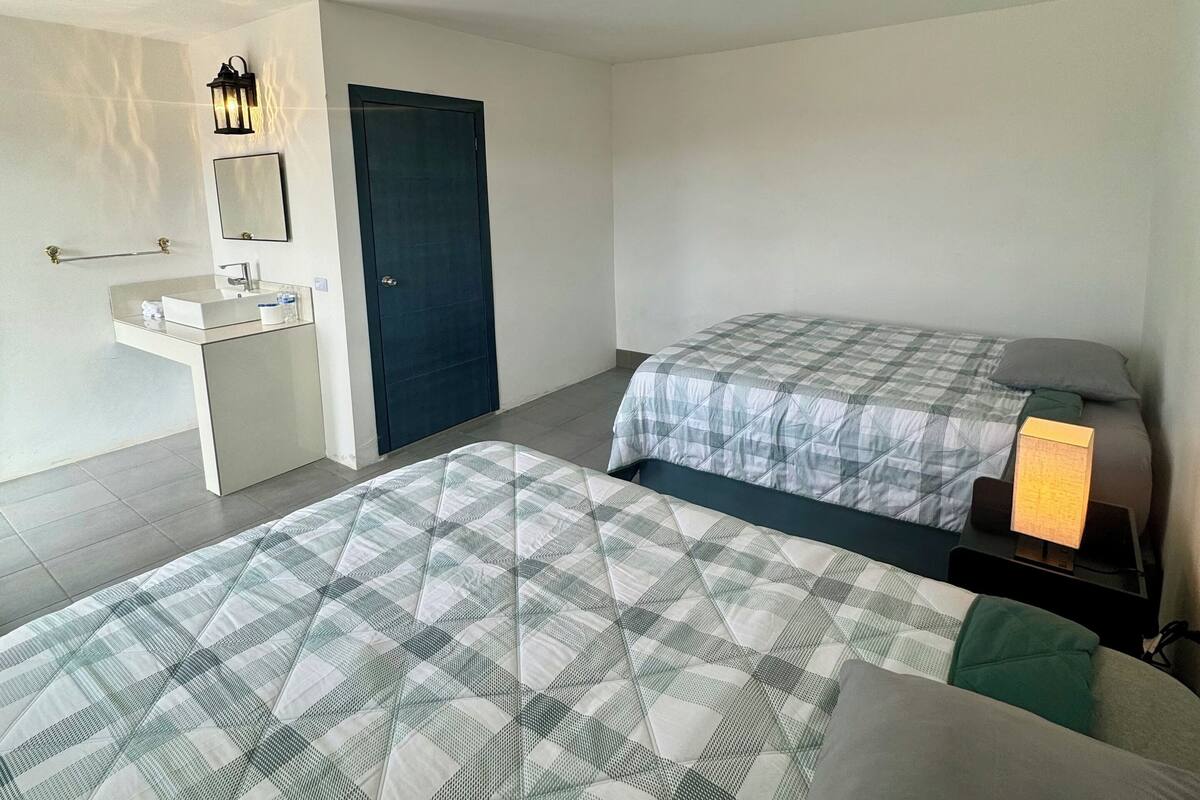 Une chambre avec deux lits, une table de chevet, un miroir, une porte et un luminaire au plafond.