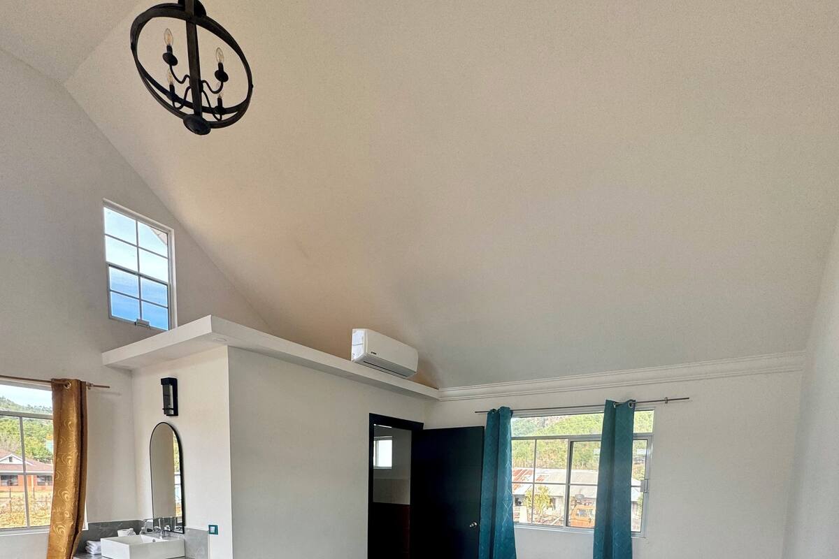 Une chambre d’hôtel avec deux lits, une coiffeuse avec un miroir, un petit tabouret, un lustre et une fenêtre avec des rideaux.