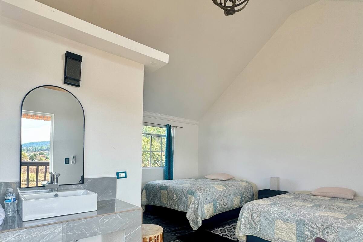 Une chambre à coucher avec un grand lit, une table de chevet, un miroir et un luminaire suspendu.