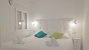 A neatly made bed with white linens, two pillows, and rolled towels. There is a bedside table with a lamp and a small drawer. - Luxurious Firstline apartment on the beach in central Nerja (Nerja)