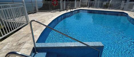 A swimming pool with tiled steps and a white metal railing.
