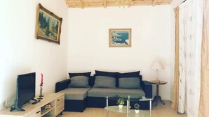 Una sala de estar con un sofá, un televisor, una mesa de centro de vidrio y dos cuadros en la pared.