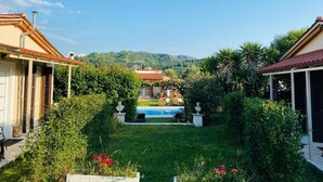 Una villa con piscina, rodeada de abundante vegetación y colinas al fondo.