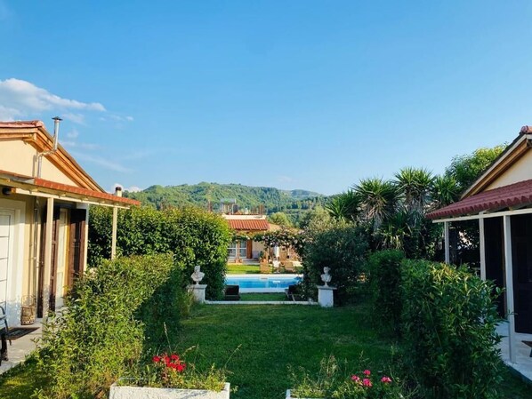 A villa with a swimming pool, surrounded by lush greenery and hills in the background.
