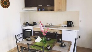 Una cocina compacta con estufa, horno y pileta, un refrigerador pequeño, y un comedor con una mesa lista para dos.