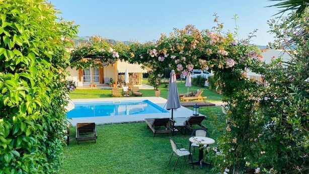 Un jardín trasero con piscina, un pérgola cubierta de flores y mobiliario exterior.