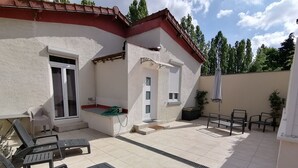 A patio area with a white exterior, a sliding glass door, and a small window. There are two lounge chairs and a table with chairs. - Maison Antony, air-conditioned, free parking  (Antony)