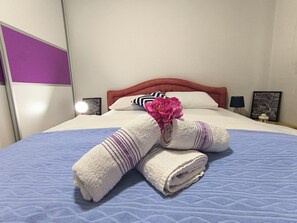 Una cama bien hecha con colcha azul, almohadas blancas y una flor rosa.