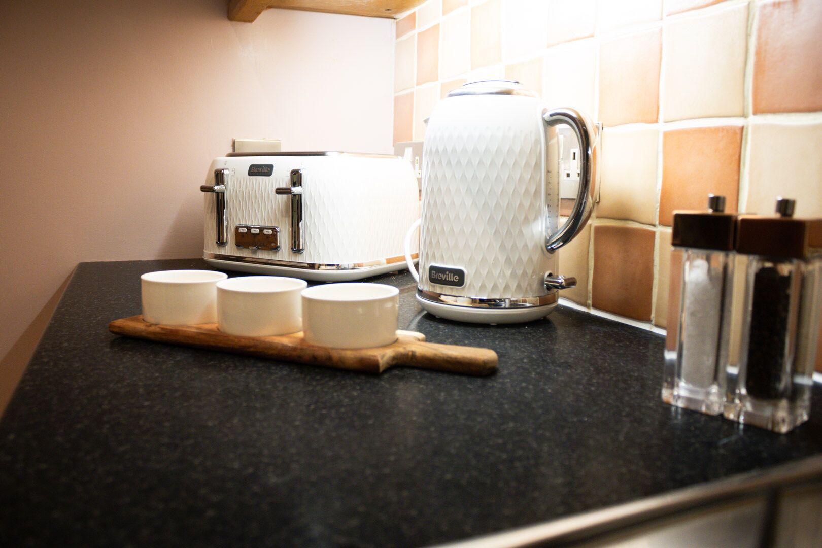Een keukenblad met een Breville broodrooster, een Breville koffiezetapparaat en drie witte bekers op een houten plank.
