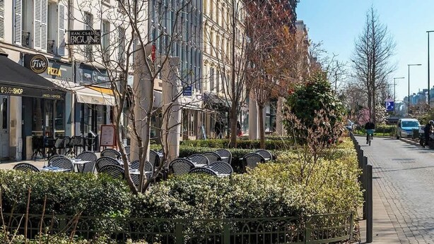 A street with outdoor seating, a pizza shop, and a building with a sign that reads 'JEAN-CLAUDE BIGUINE.'