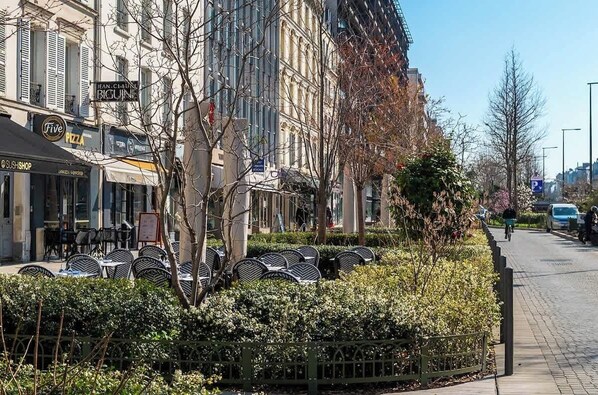 A street with outdoor seating, a pizza shop, and a building with a sign that reads 'JEAN-CLAUDE BIGUINE.'