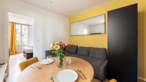 A modern living room with a round dining table, a sofa, a large mirror, and a yellow accent wall.
