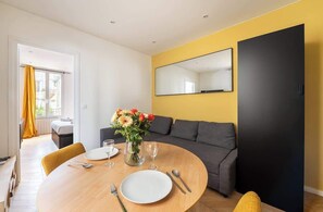 A modern living room with a round dining table, a sofa, a large mirror, and a yellow accent wall.