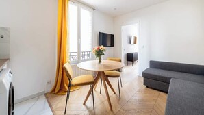 A modern living room with a round wooden table, yellow chairs, a grey sofa, and a TV mounted on the wall.