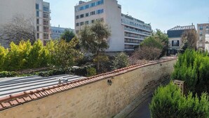 A multi-story building with a flat roof, surrounded by greenery and a stone wall.