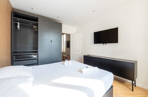 A modern hotel room with a bed, a wardrobe, a TV, and a radiator. - Mobility lease l Equipped & Paris 10 mins away (Neuilly-sur-Seine)