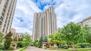 A high-rise residential building with a central entrance, surrounded by greenery and other buildings.