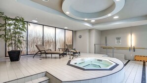 A modern indoor pool area with a hot tub, lounge chairs, and a large potted plant.