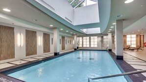 An indoor swimming pool with a skylight, tiled walls, and a sunlit area with lounge chairs.