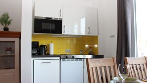 A compact kitchen with a microwave, dishwasher, and a dining area with wooden chairs and a table set for two. - Hexenquartier apartment in a central location in Braunlage (Braunlage)