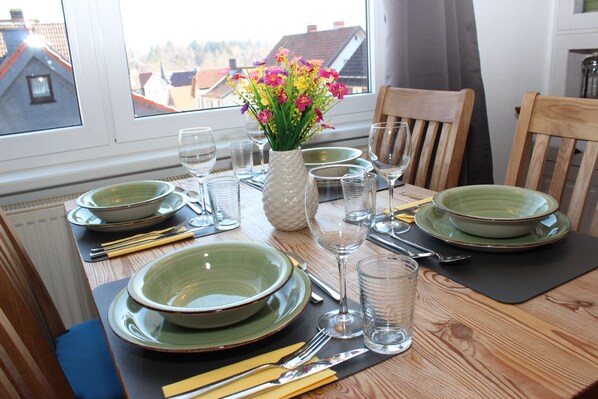 A dining table set with green plates, bowls, cutlery, and a vase of flowers.