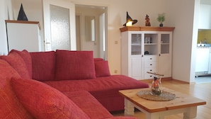 A living room with a red sofa, a wooden coffee table, and a white cabinet with glass doors. - Hexenquartier apartment in a central location in Braunlage (Braunlage)
