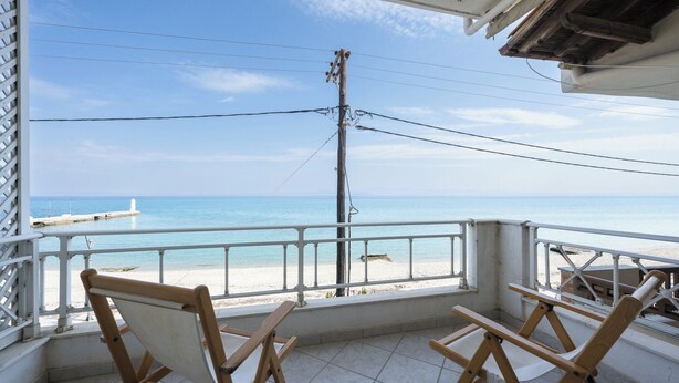 A balcony with a view of the beach and the sea. There are two wooden chairs and a table. - Pefkohori Blue View by Luxlikehome (Pefkochori Halkidiki)