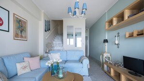 A living room with a blue sofa, a coffee table with flowers, a TV, and a bookshelf. - Pefkohori Blue View by Luxlikehome (Pefkochori Halkidiki)