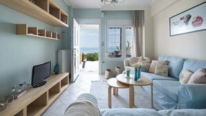 A living room with a sofa, a coffee table, and a TV. There is a view of the sea through a window. - Pefkohori Blue View by Luxlikehome (Pefkochori Halkidiki)