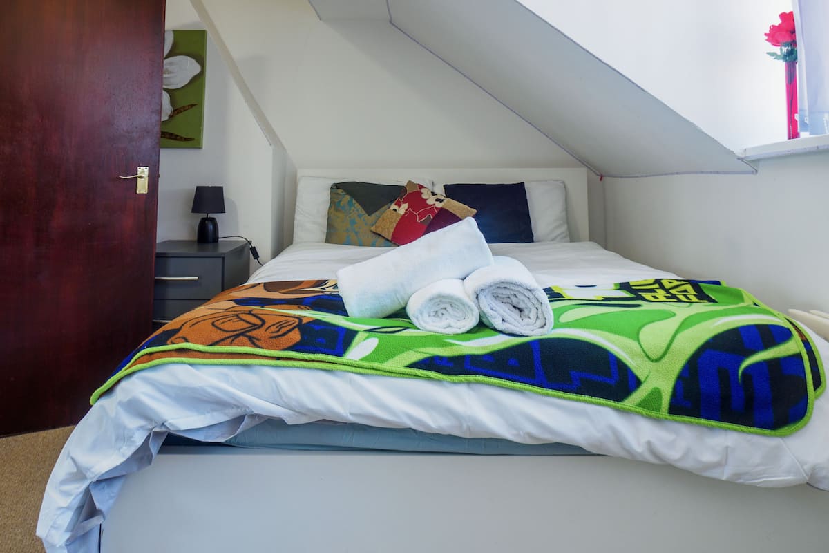 A neatly made bed with a colorful blanket, a pillow with a floral pattern, and a rolled towel on the bed.