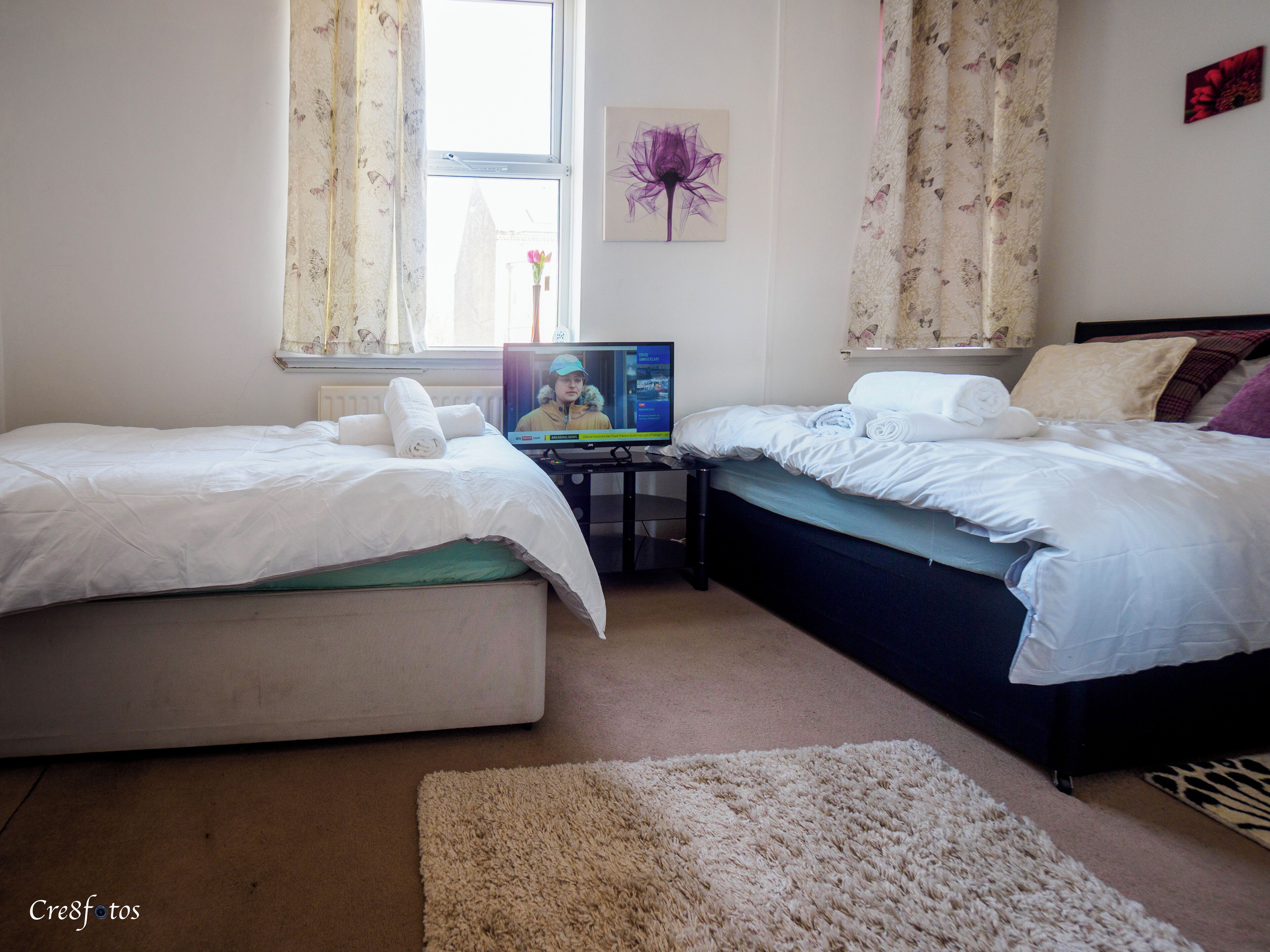 Un dormitorio con dos camas, televisión y una ventana con cortinas.